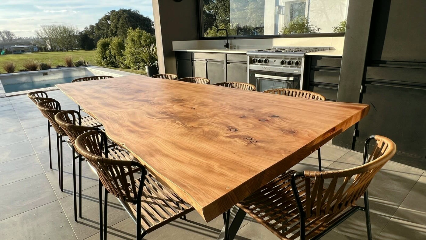 Mesa de madera maciza con sillas trenzadas frente a una galería con pileta